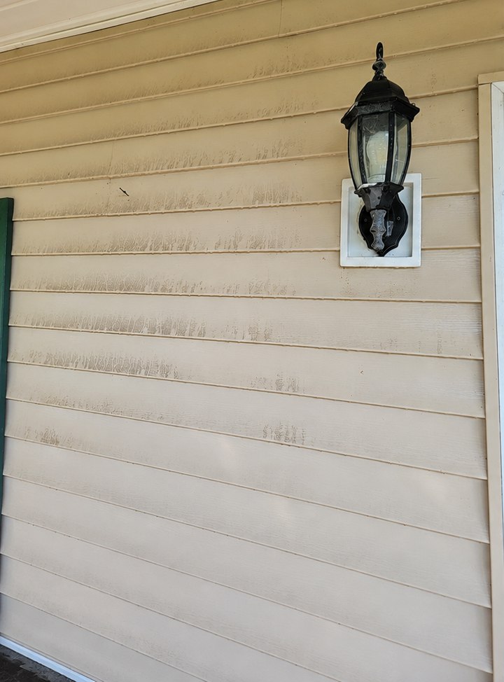 Faded, weather-streaked exterior siding beside a porch light before refinishing